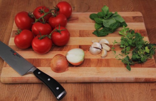 Zutaten für Tomatensoße bestehend aus frischen Rispentomaten, Basilikum, Oregano, Knaublauch und einer Zwiebel.