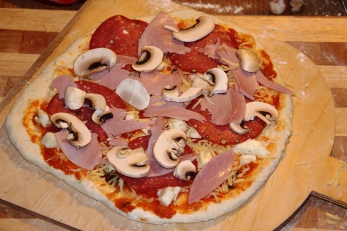 Pizza Speciale vor dem Backen. Diese rohe Pizza enthält Schinken, Salami und Pilze neben frischer Tomatensoße und Mozzarella-Käse.